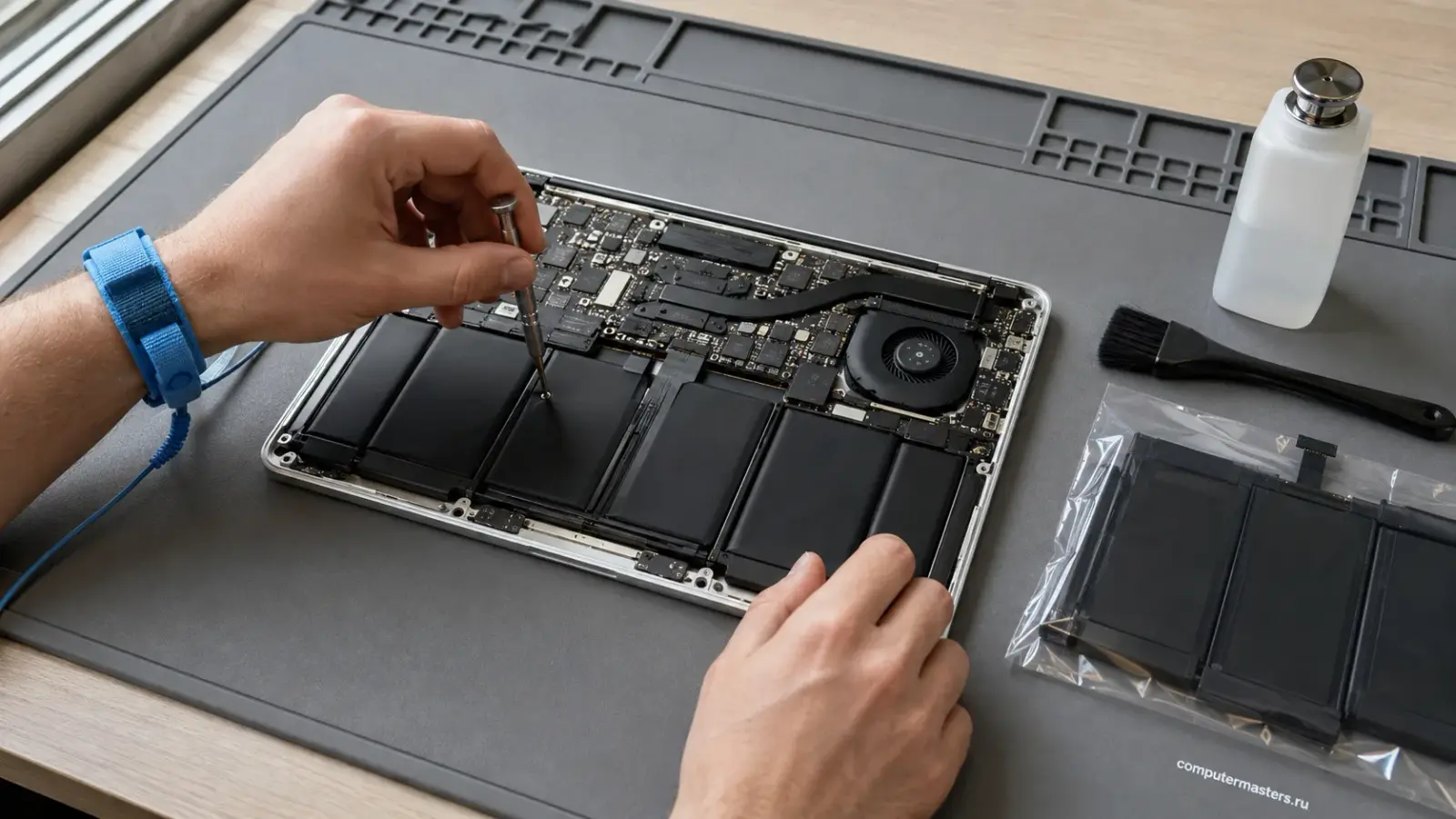 MacBook со снятой нижней крышкой на столе мастера, рядом инструмент для работы с платой