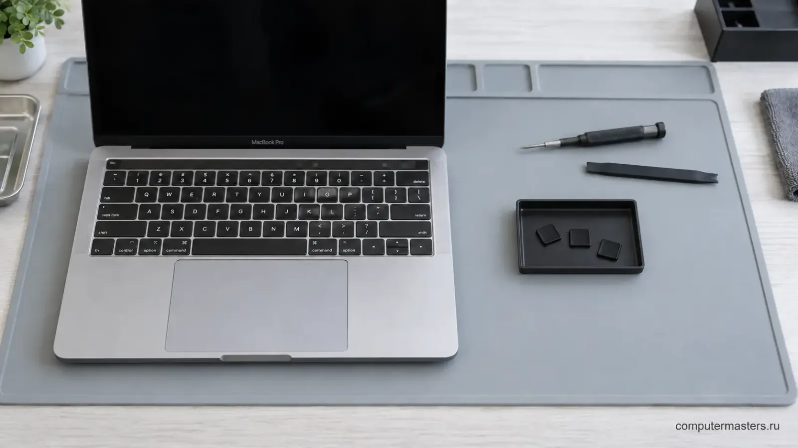 MacBook с открытой крышкой и чёрным экраном; рядом отдельные колпачки клавиш и инструмент для осмотра