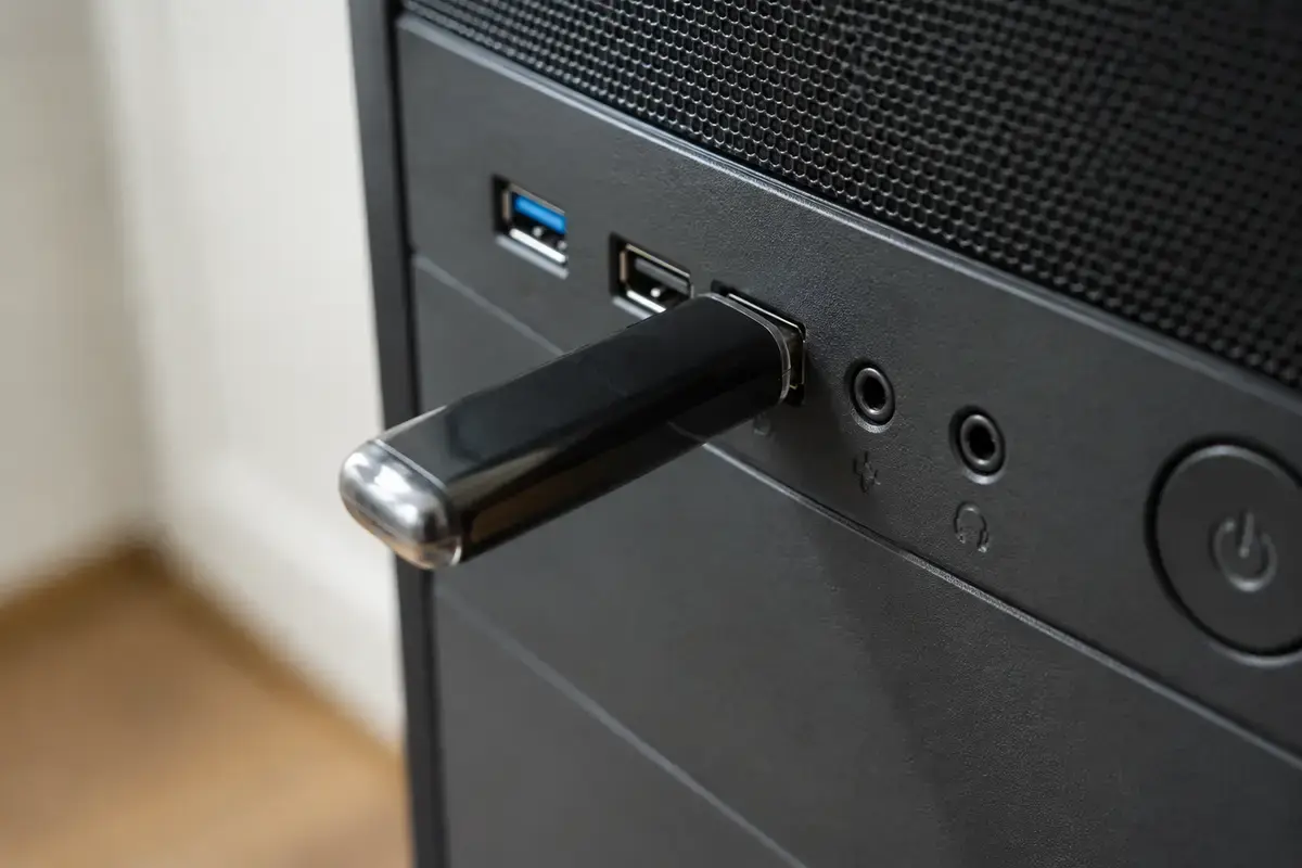 Чёрная флешка вставлена в передний USB-порт системного блока, рядом гнёзда для наушников и микрофона