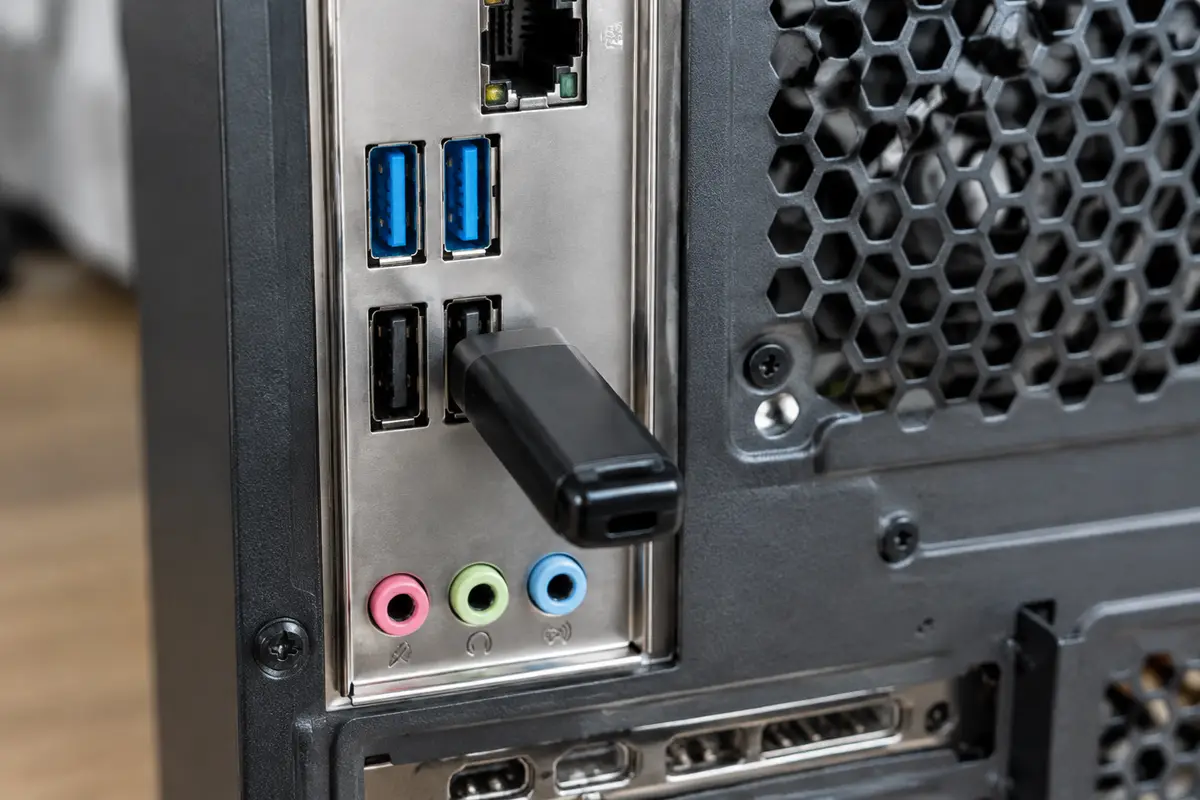 Задняя панель системного блока с синими и чёрными портами USB, в чёрный порт вставлена флешка
