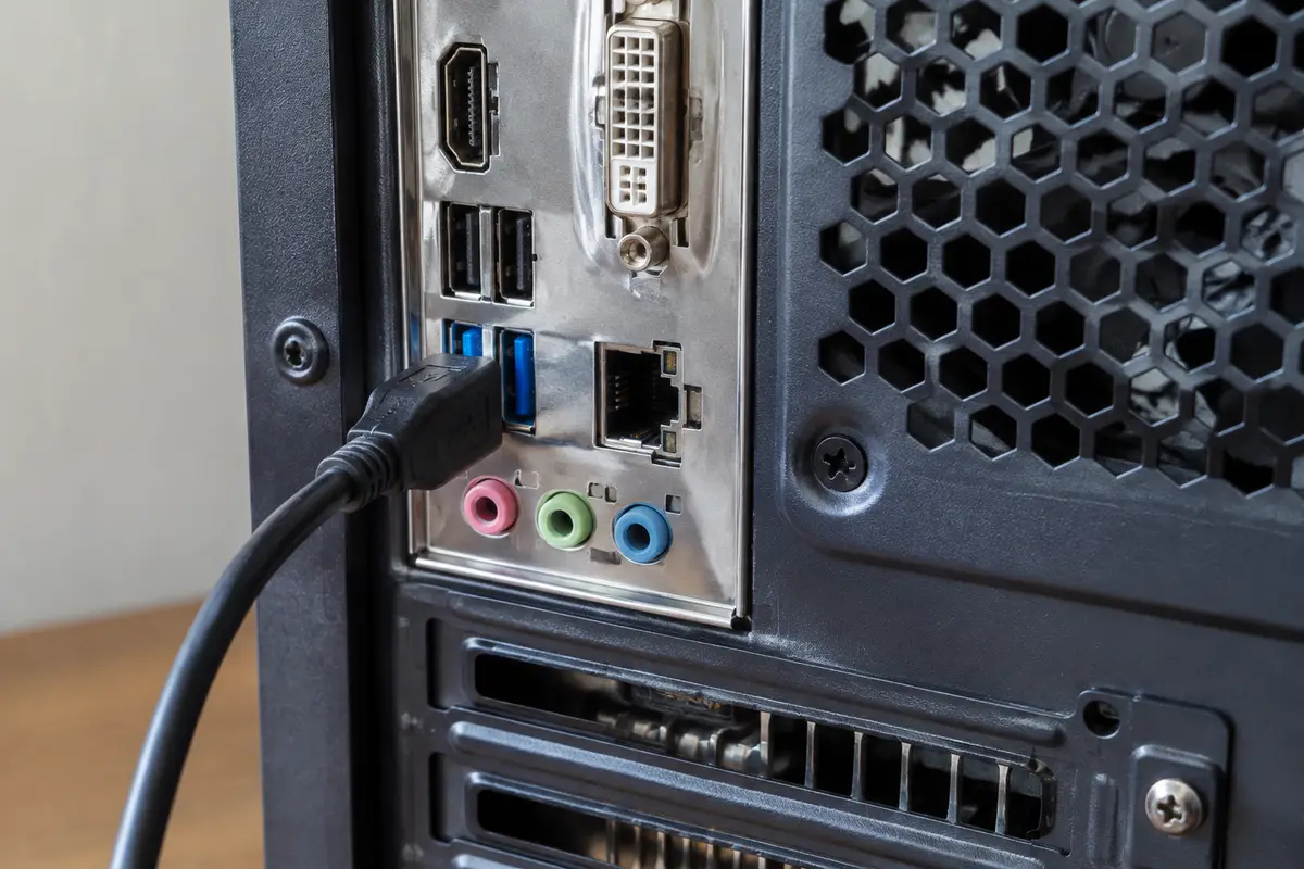 Задняя панель системного блока, чёрный USB-кабель вставлен в синий порт USB 3.0 рядом с сетевым разъёмом и аудиовыходами